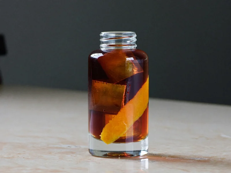 Cold Brew in klarer Glasflasche mit Eis und Orangenschale auf Steinplatte