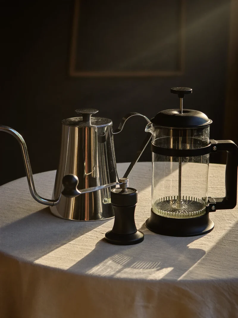 Schwanenhalskessel, Handmühle und French Press auf hellem Leinentuch
